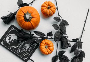 Halloween-themed flatlay with pumpkins, black roses, and a moon-themed card for spooky decor.